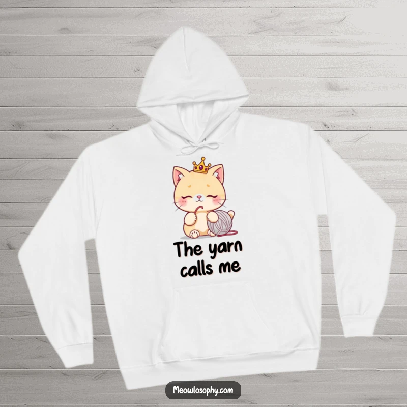 Funny hoodie with a cute cat wearing a tiny crown, looking thoughtfully at a yarn ball, warm and humorous cat lover clothing.